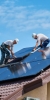 Monteure schleppen ein Solarmodul auf einem Dach