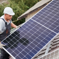 Photovoltaik Monteur auf dem Dach mit einer Solarpanele in der Hand