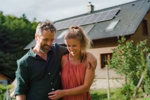 Glückliches Paar in den Armen vor einem Haus mit Photovoltaik auf dem Dach