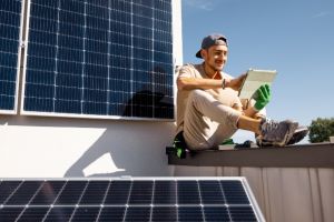 Junger Mann auf einem Dach mit Photovoltaikanlagen mit einem Tablet in der Hand