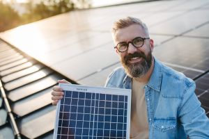 Älterer Mann mit einem PV-Moduk auf einem Schrägdach mit Photovoltaik-Paneelen